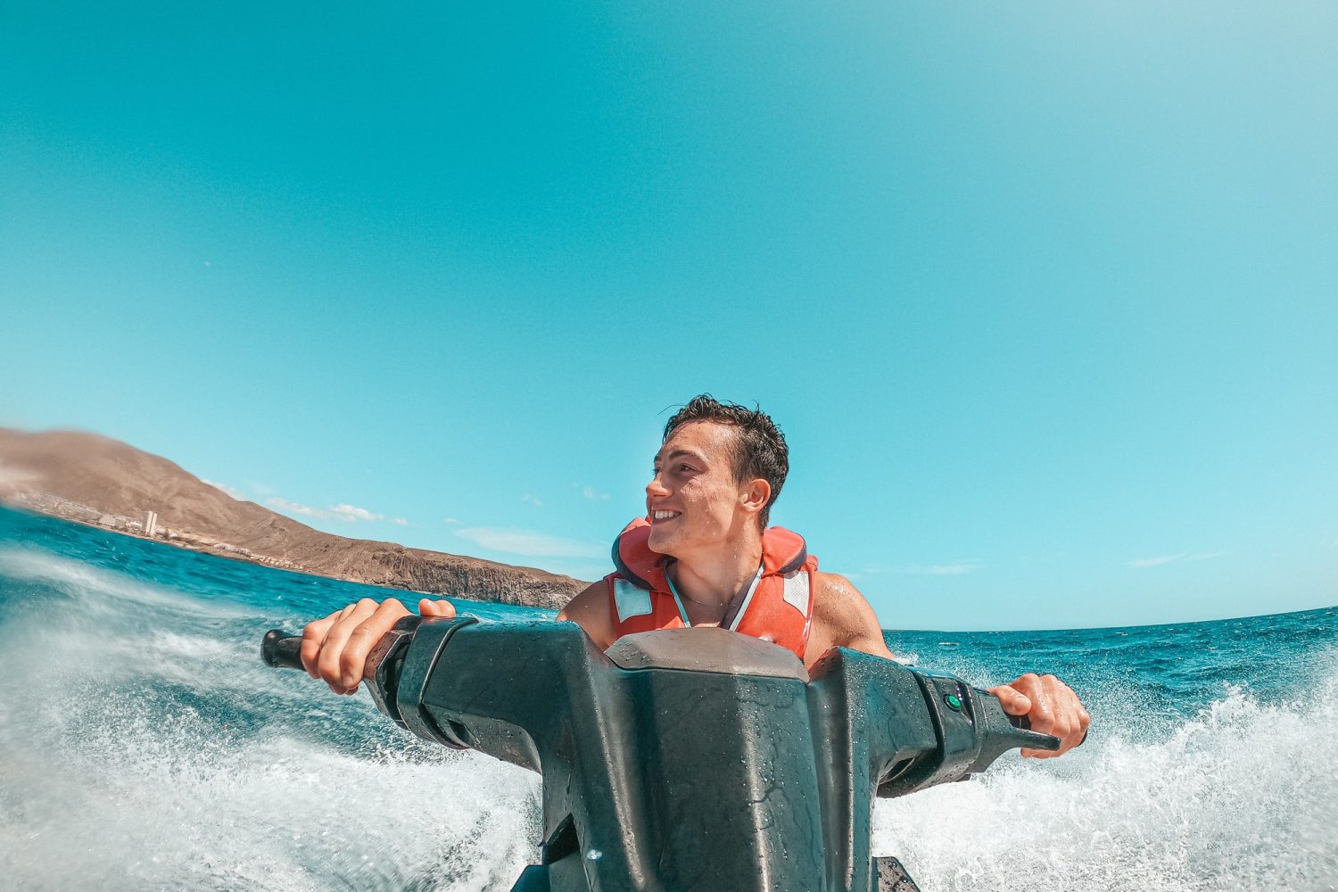 Teenager man enjoying summer in a jet ski in the middle of the sea having fun